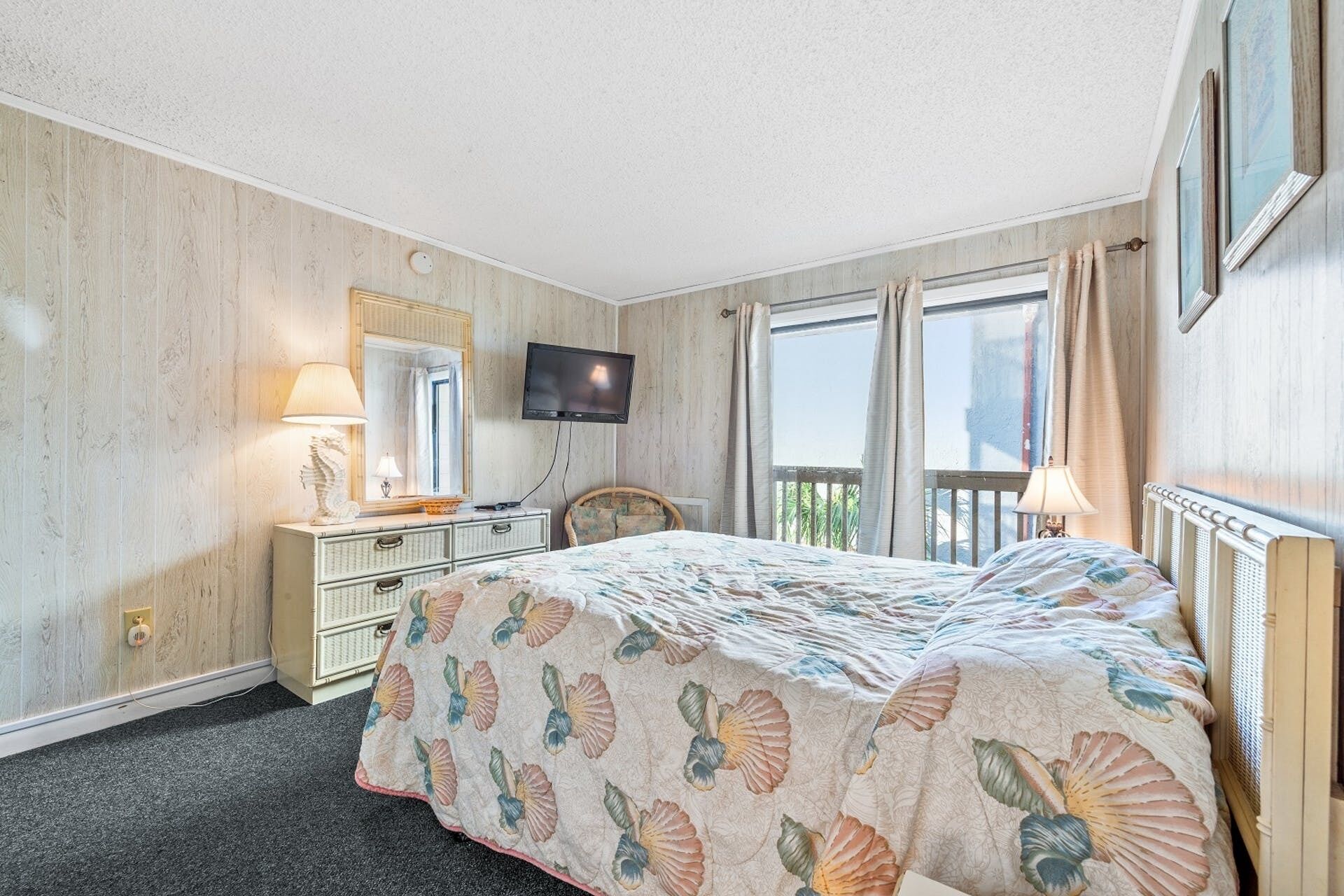 A hotel room with a bed, a dresser, a television, and a window with curtains.