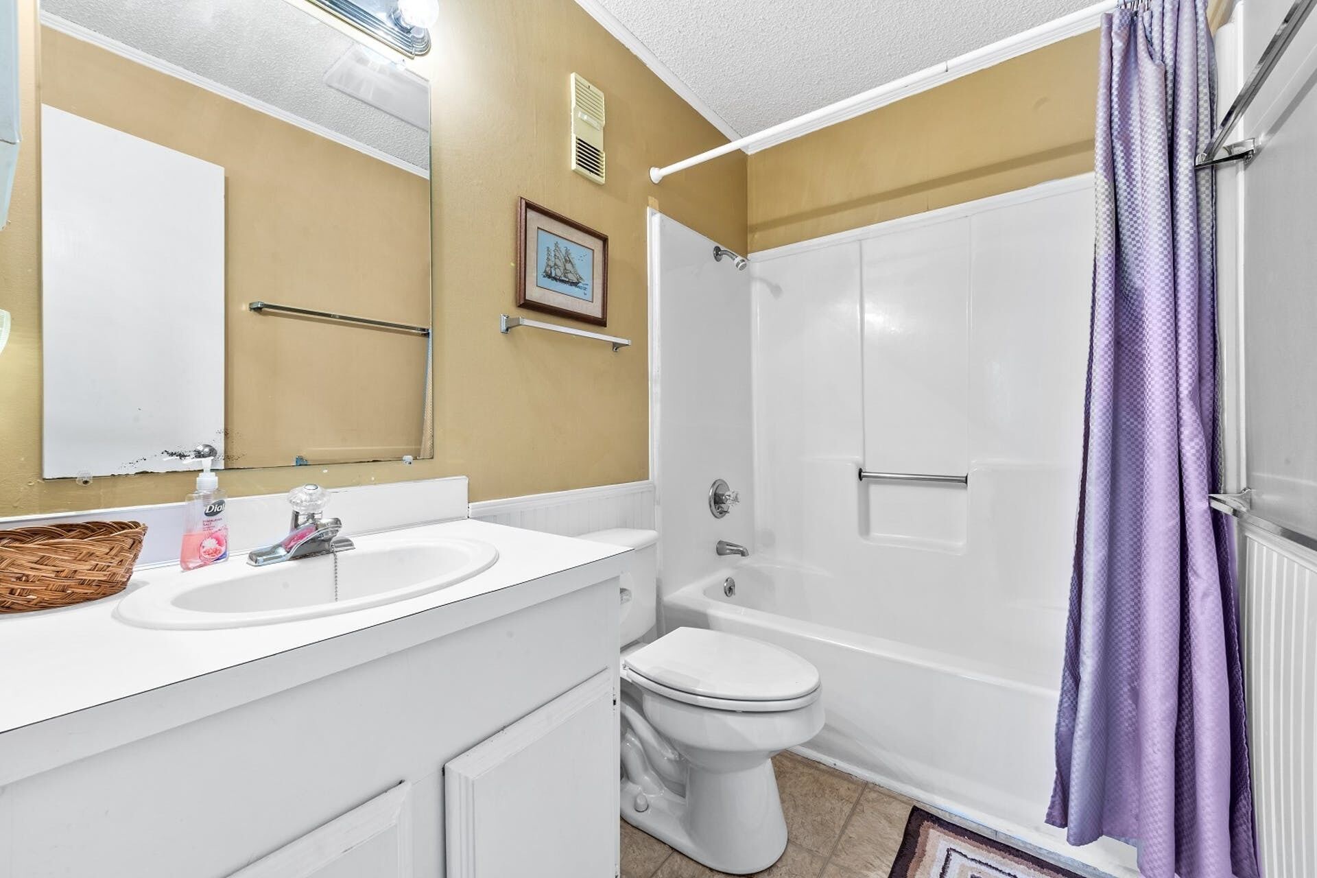 Un baño con lavamanos blanco, inodoro y ducha con cortina púrpura.