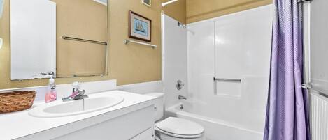 A bathroom with a white sink, a toilet, and a shower with a purple curtain.