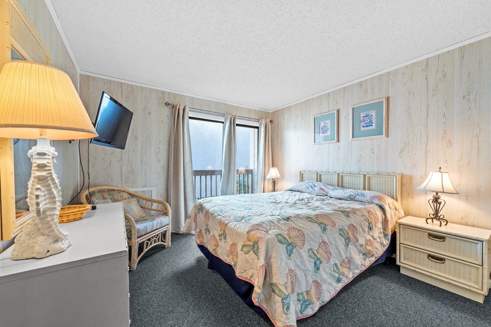 Habitación de hotel con cama, escritorio, silla, televisor y balcón.