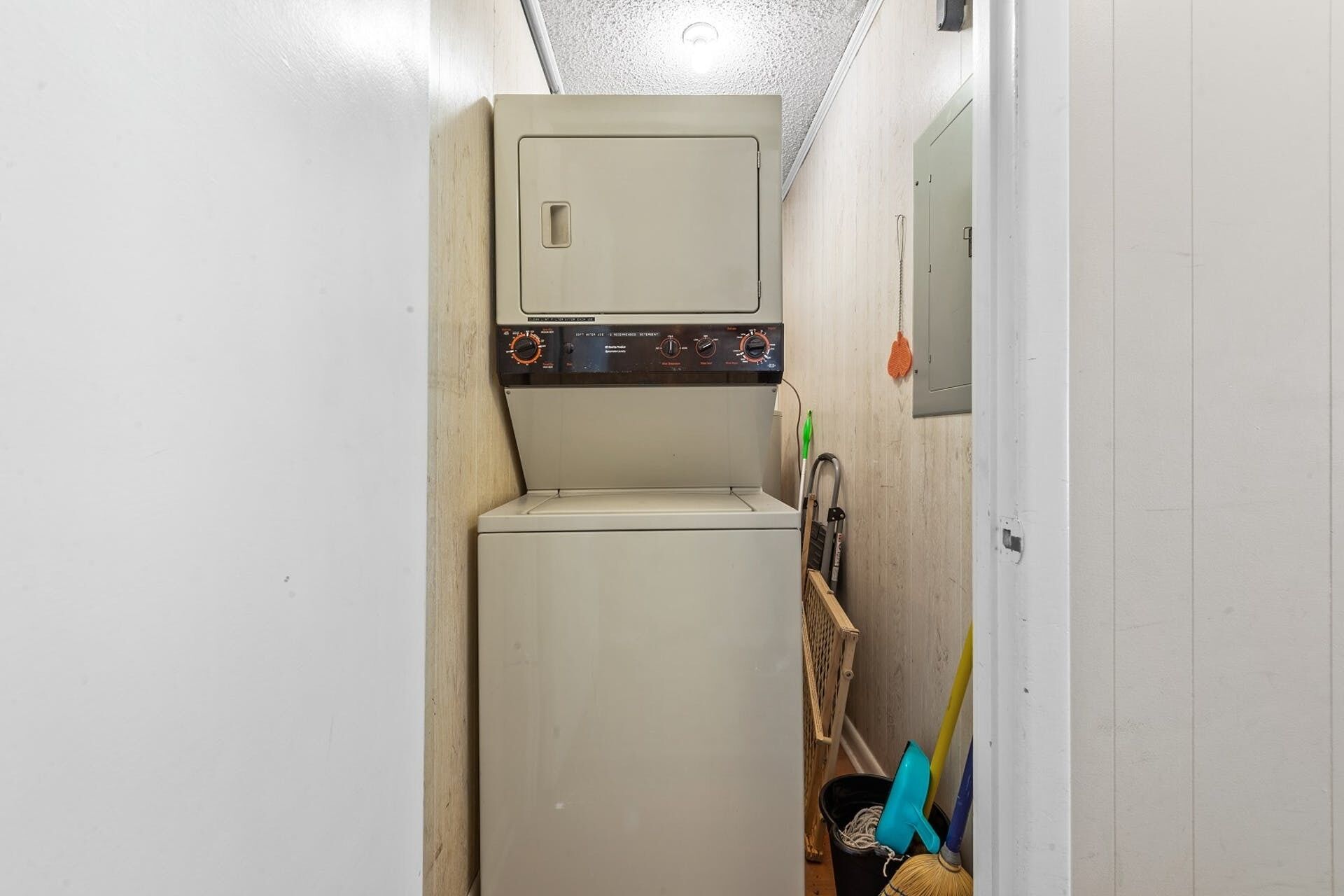 A compact laundry room with a washing machine and dryer, a broom, and a mop leaning against the wall.