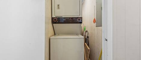 A compact laundry room with a washing machine and dryer, a broom, and a mop leaning against the wall.