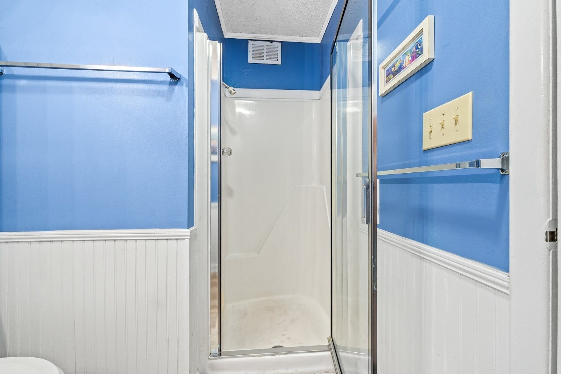 A bathroom with a glass shower enclosure, white walls, and blue trim.