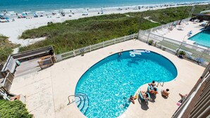 A pool with clear blue water, surrounded by a deck area with lounge chairs and umbrellas. - Two bedroom, two-bathroom oceanfront condo | Crescent Beach Villas - 201 (North Myrtle Beach)