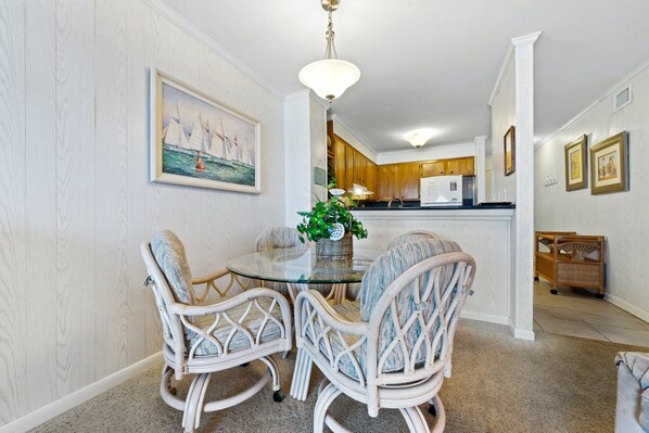 A dining area with wicker chairs, a glass table, and a painting of sailboats on the wall.