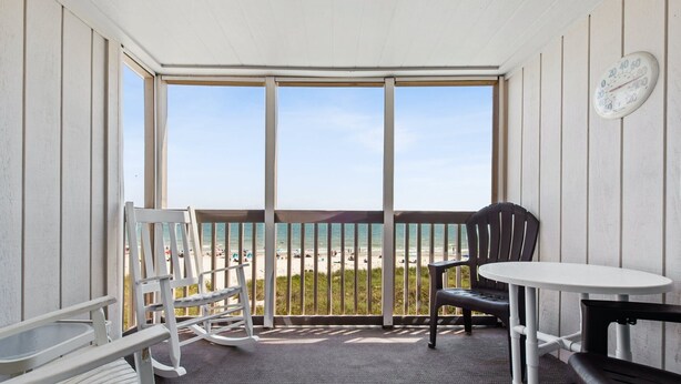 Un balcon avec vue sur la plage, une table ronde et deux chaises.