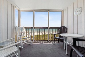 A balcony with a view of the beach, a round table, and two chairs.