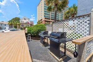 Un espace patio aménagé avec un barbecue, une table en bois et une clôture blanche en treillis.