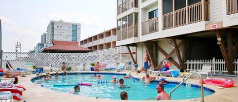 A swimming pool area with lounge chairs and a building with balconies.