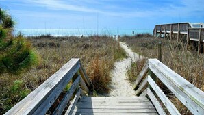 A wooden boardwalk leading to a beach with a fence and a wooden structure in the background. - 2-bedroom Corner Unit with private balcony | Carolina Reef - 301 (North Myrtle Beach)