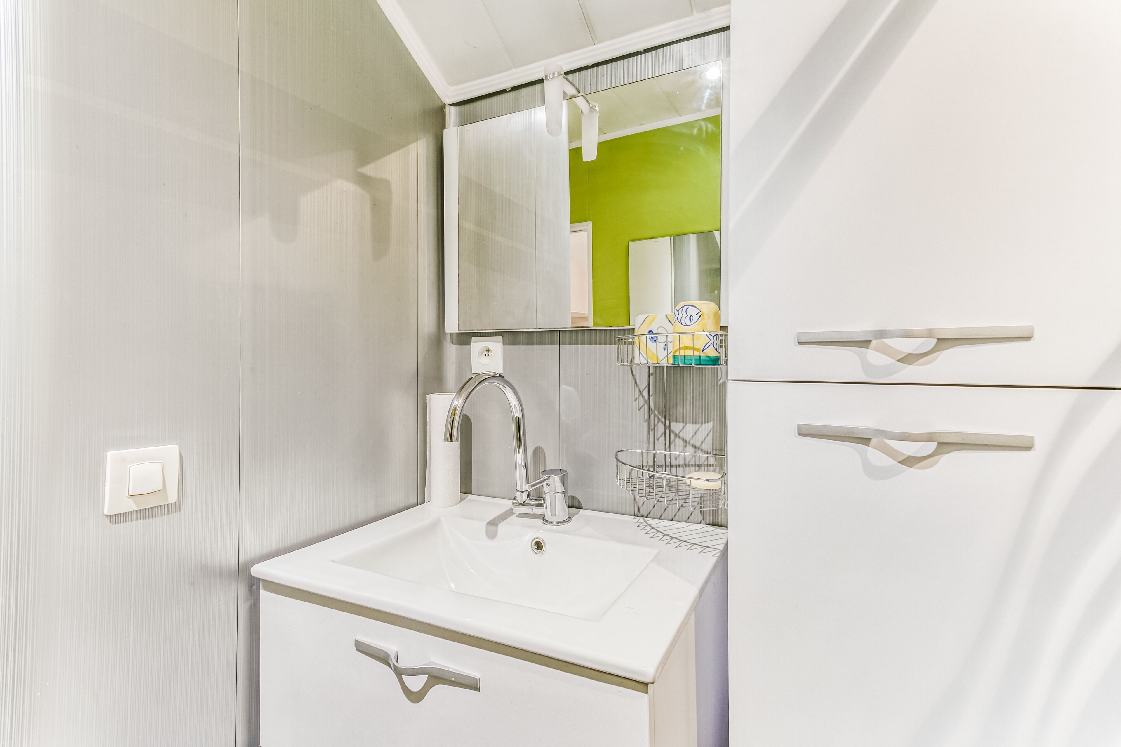 Un baño moderno con un lavamanos blanco, un espejo y una pared de acento verde.
