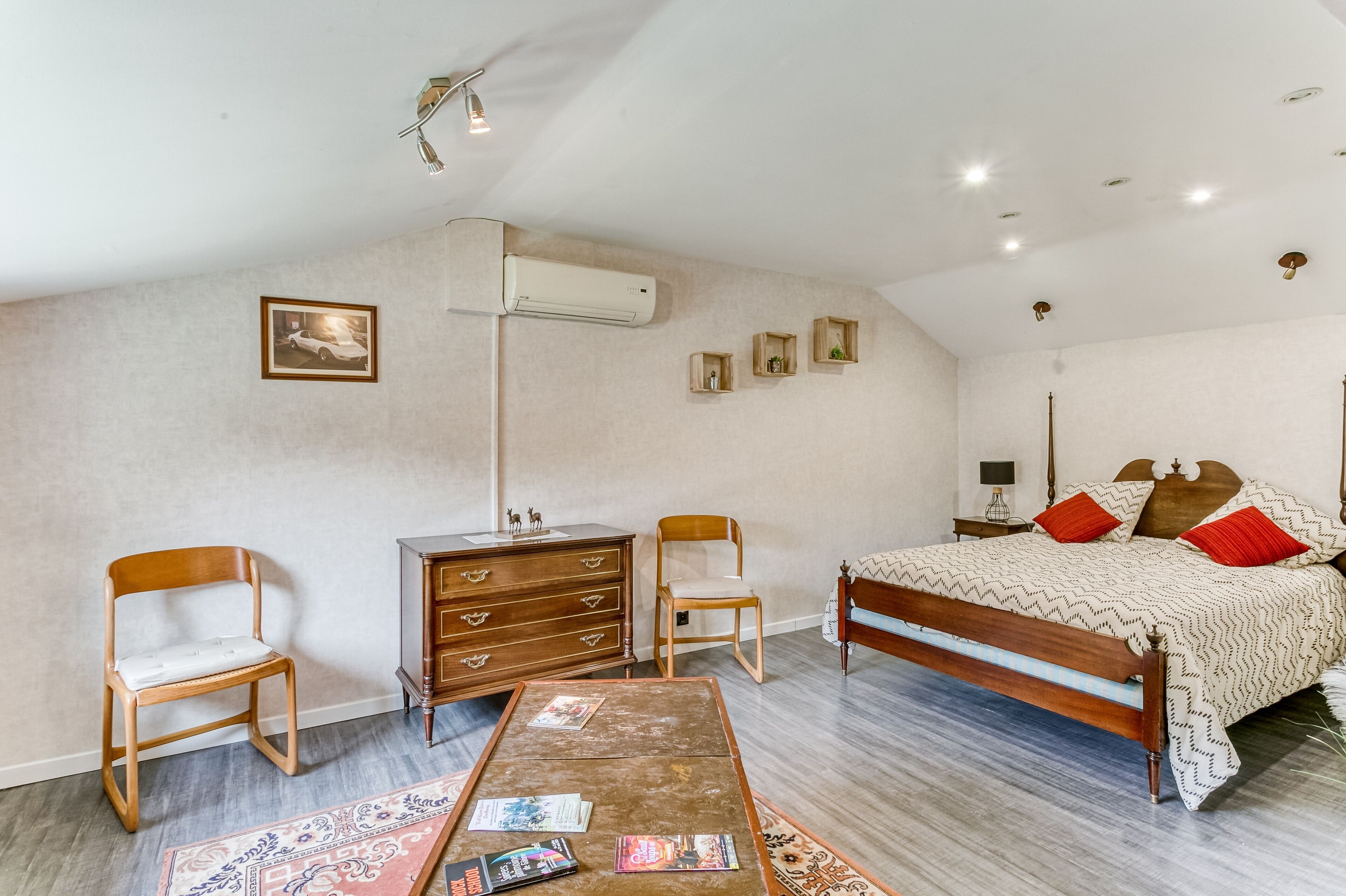 A bedroom with a bed, two wooden chairs, a small table, a dresser, and a wall-mounted air conditioner.
