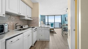 A modern kitchen with white cabinets, a stove, and a dishwasher. There is a balcony with a view of the sea. - Updated 1-Bedroom Oceanfront Condo| Carolina Reef - 704 (North Myrtle Beach)