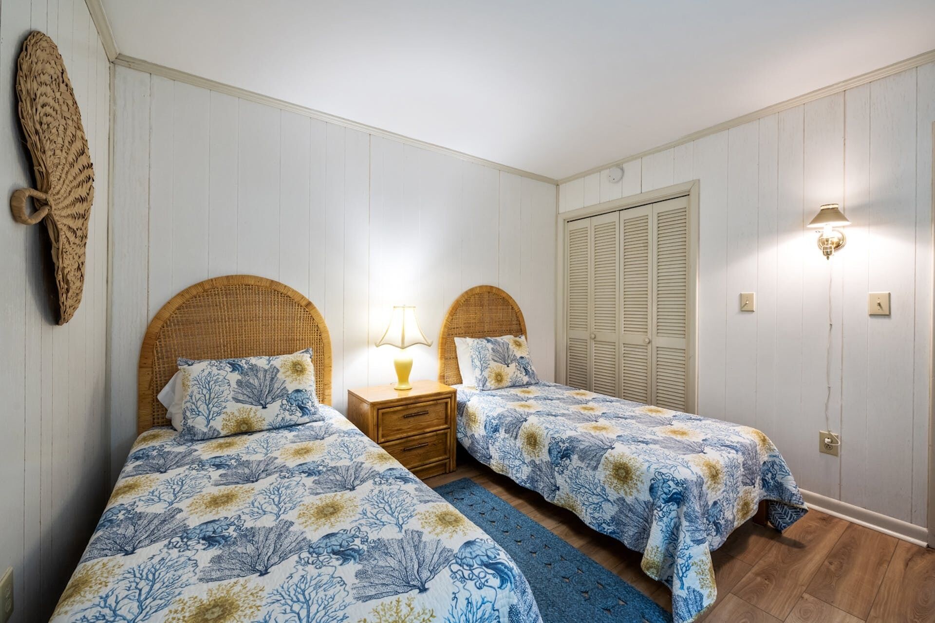 A bedroom with two single beds, a nightstand with a lamp, a large closet, and a wall-mounted decorative item.