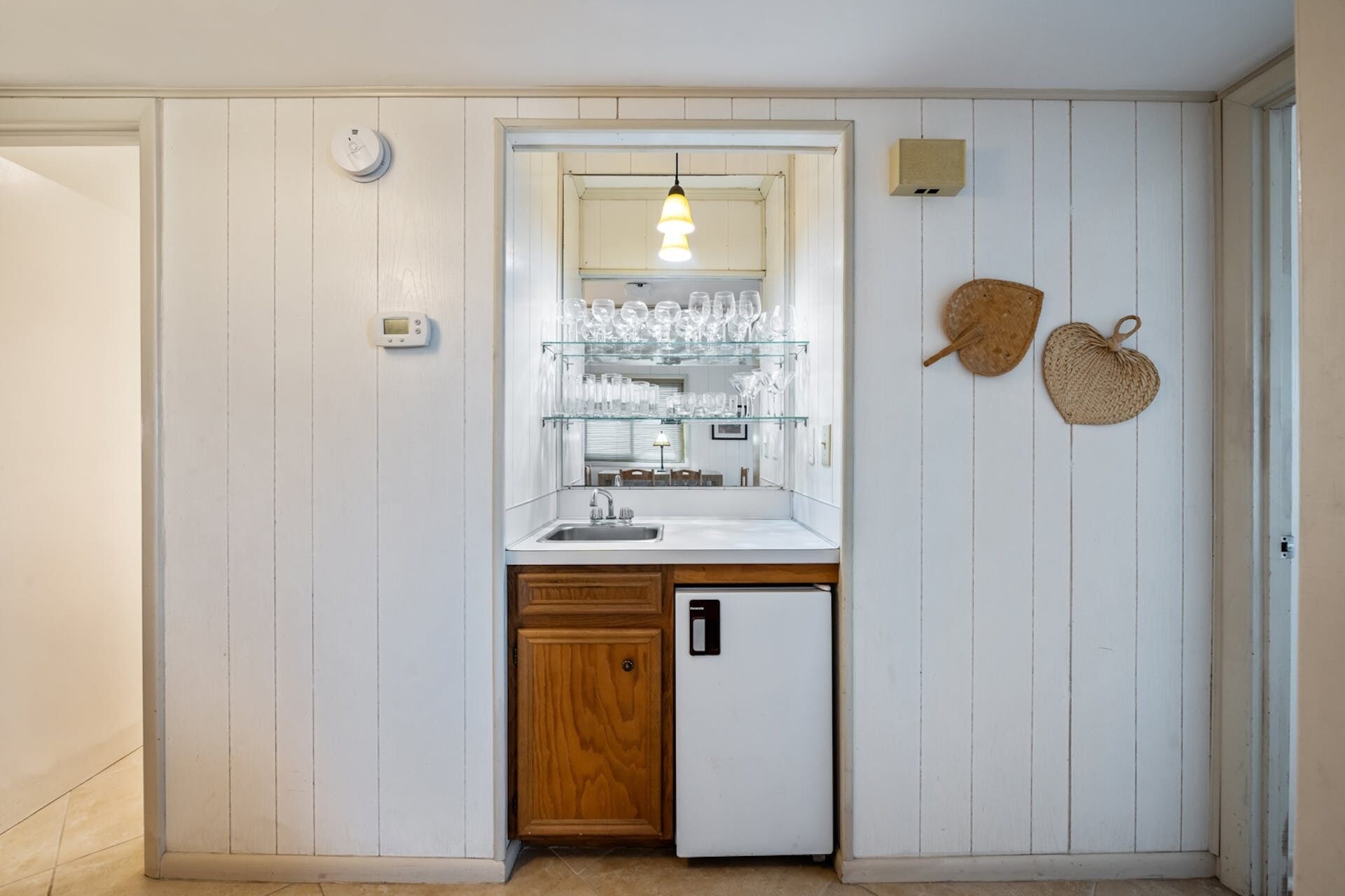 A compact kitchen with a built-in refrigerator, a sink, and a glass display shelf for dishes.