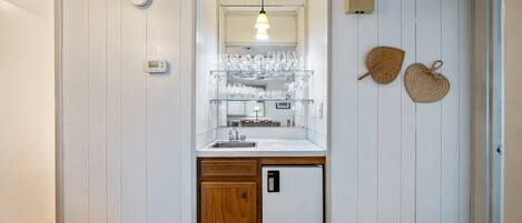 A compact kitchen with a built-in refrigerator, a sink, and a glass display shelf for dishes.