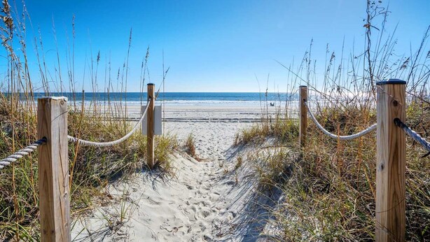 A sandy beach path leading to the ocean, surrounded by wooden posts and rope barriers. - 3-bedrom, 2.5 bath, 1st floor oceanfront condo | Dunescape - 101 (North Myrtle Beach)