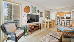 A living room with a TV, wicker furniture, and a dining area with wooden chairs and a table. - 3-bedrom, 2.5 bath, 1st floor oceanfront condo | Dunescape - 101 (North Myrtle Beach)