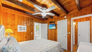 A wooden-paneled room with a bed, a ceiling fan, and a television on the wall. - 3-bedroom Beach Cottage, 4th Row, Large Back Deck and screened in porch | Mermaid Cottage - 4000 (North Myrtle Beach)