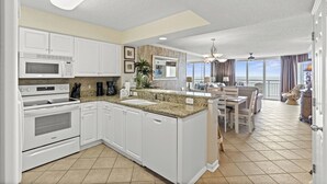 A modern kitchen with white cabinets, a granite countertop, and a dining area with a view of the ocean. - Elegant oceanfront 3-bed, 3-bath condo | South Shore Villas - 706nt Crescent Beach 2K 2Q   SS (North Myrtle Beach)