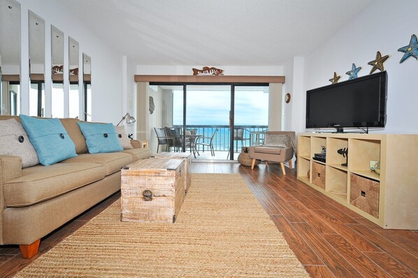 A living room with a sofa, a coffee table, a TV, and a balcony with a view. - Upscale 4th floor, 3-bed, 3-bath oceanfront condo | Crescent Tower II - 407 (North Myrtle Beach)