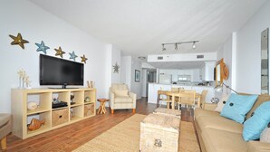 En stue med tv, sofa, sofabord og et spiseområde med stole og bord.