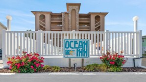 A sign for Ocean Inn with a white fence and pink flowers in front. - Renovated 1-bedroom, 1-bath 3rd floor oceanfront condo | Ocean Inn - 303 (North Myrtle Beach)