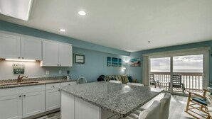 A modern kitchen with a granite countertop, white cabinets, and a view of the ocean through a large sliding glass door. - Renovated 1-bedroom, 1-bath 3rd floor oceanfront condo | Ocean Inn - 303 (North Myrtle Beach)