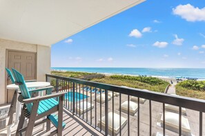 Un balcon avec vue sur la plage, une piscine et des chaises longues.