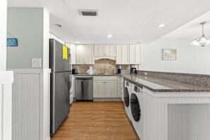 A modern kitchen with white cabinetry, stainless steel appliances, a granite countertop, and a built-in washing machine.