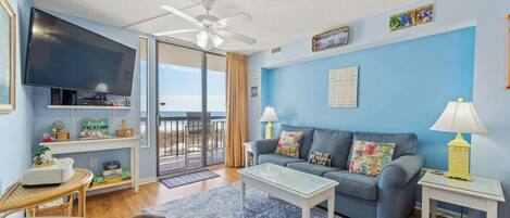 A living room with a sofa, coffee table, and television. There is a balcony with a view.