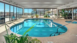 Ein Hallenbad mit großen Glaswänden, ein Poolbereich mit Liegestühlen und Blick auf die umliegenden Gebäude.