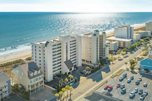 Un hotel sulla costa con diversi edifici, un parcheggio e vista sulla spiaggia.