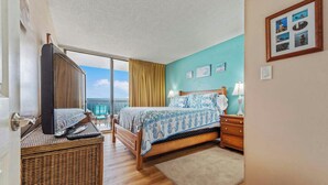 Ein Hotelzimmer mit Bett, Fernseher, Beistelltisch aus Weidwerk, Nachttisch und Meerblick.