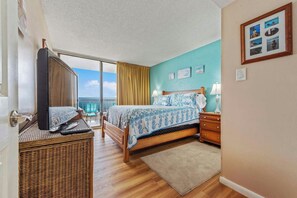 Una camera d'albergo con un letto, una televisione, un tavolino in vimini, un comodino e vista sul mare.