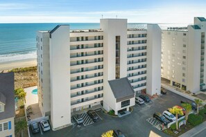 A multi-story hotel with a pool, parking, and a view of the beach.