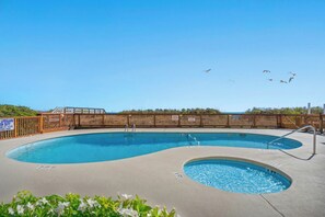 A swimming pool with a wooden fence, lifeguard duty sign, and a clear sky.