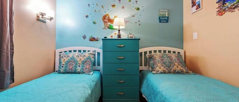 A bedroom with two single beds, a dresser, and a wall decorated with marine-themed stickers.