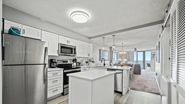 A modern kitchen with white cabinetry, stainless steel appliances, and a central island. - Calming paint palette and stylish design, 3-bedroom, 3-bath, sleeps 8, oceanfront condo | Summit -3D (North Myrtle Beach)