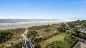 A beach view with a pathway leading to a building with a covered patio area. - Calming paint palette and stylish design, 3-bedroom, 3-bath, sleeps 8, oceanfront condo | Summit -3D (North Myrtle Beach)