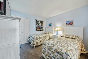 A bedroom with two beds, a wardrobe, and a nightstand with a lamp.