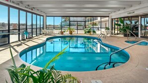 Une piscine intérieure avec des parois en verre transparent, une table de billard et des plantes en pot.