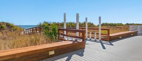 Un malecón de madera que conduce a una playa, con un banco de madera y una valla blanca.