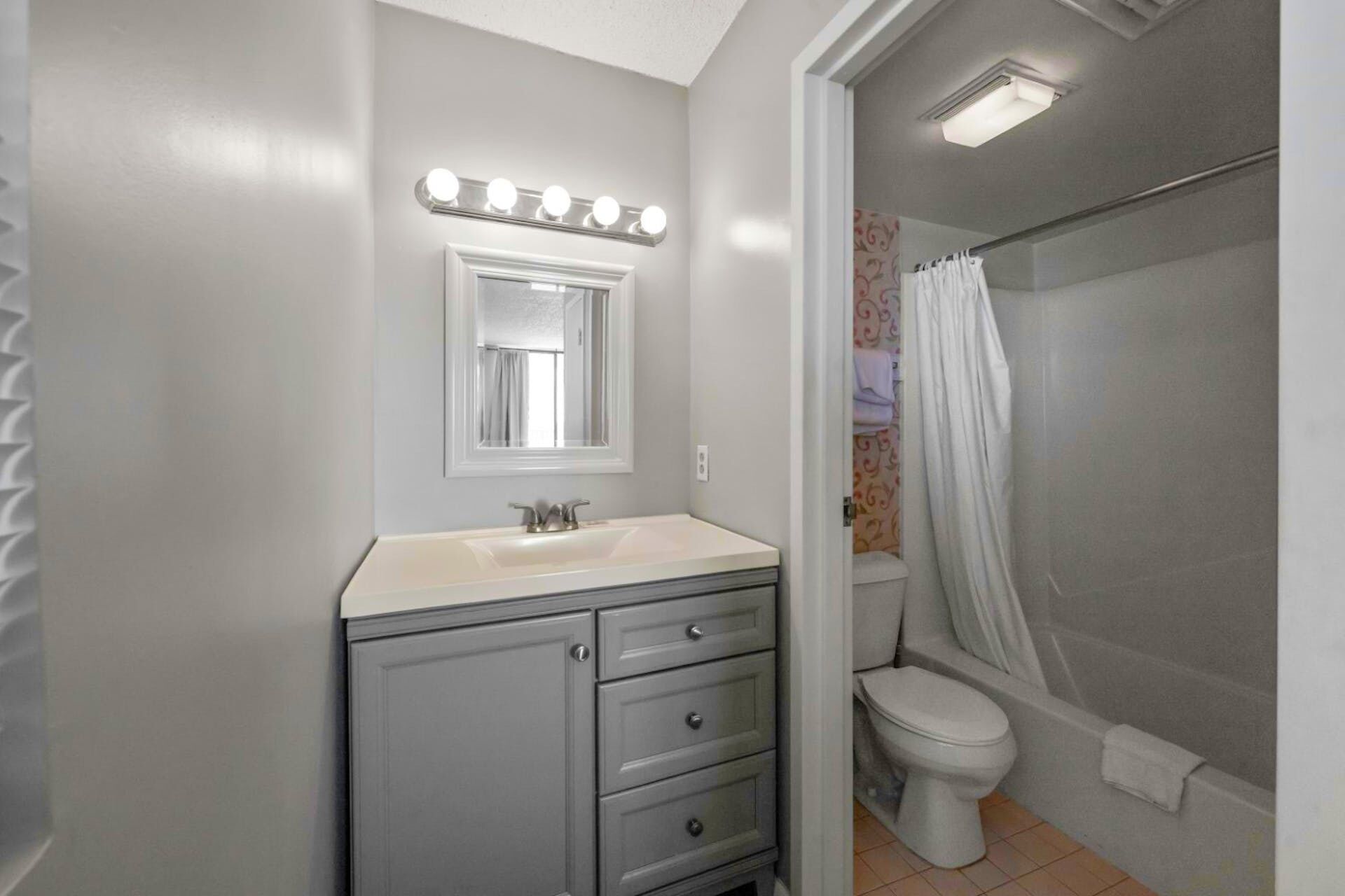 A bathroom with a vanity, a mirror with lights, a toilet, and a shower.