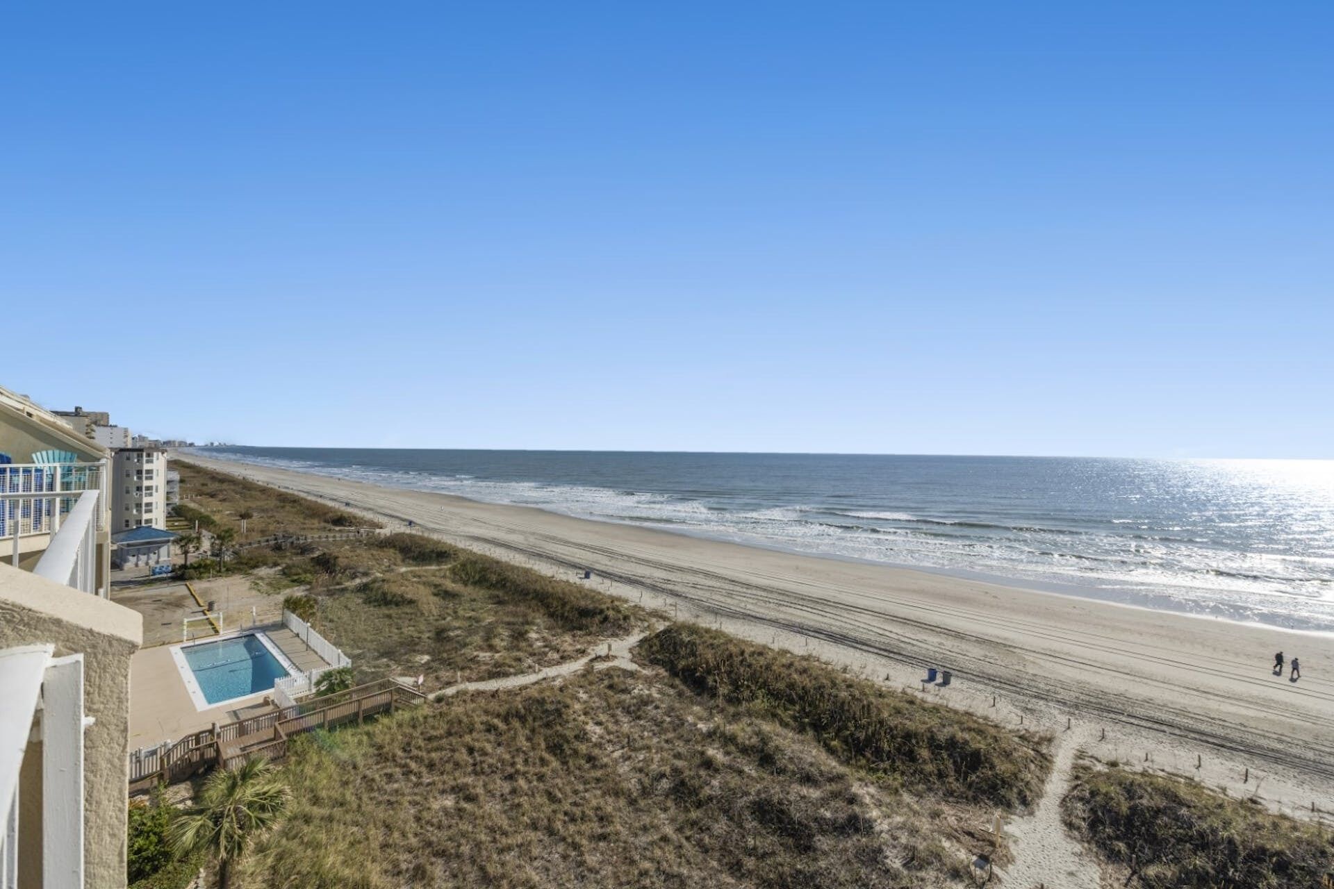 A beach view with a swimming pool, beach chairs, and a path leading to the shore.