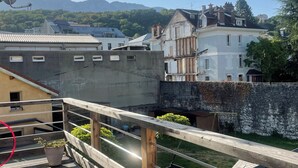 A wooden deck with a railing, potted plants, and a view of buildings and greenery in the background. - Quiet, bright apartment, 400 metres from the town center, with parking lot (Aix-les-Bains)