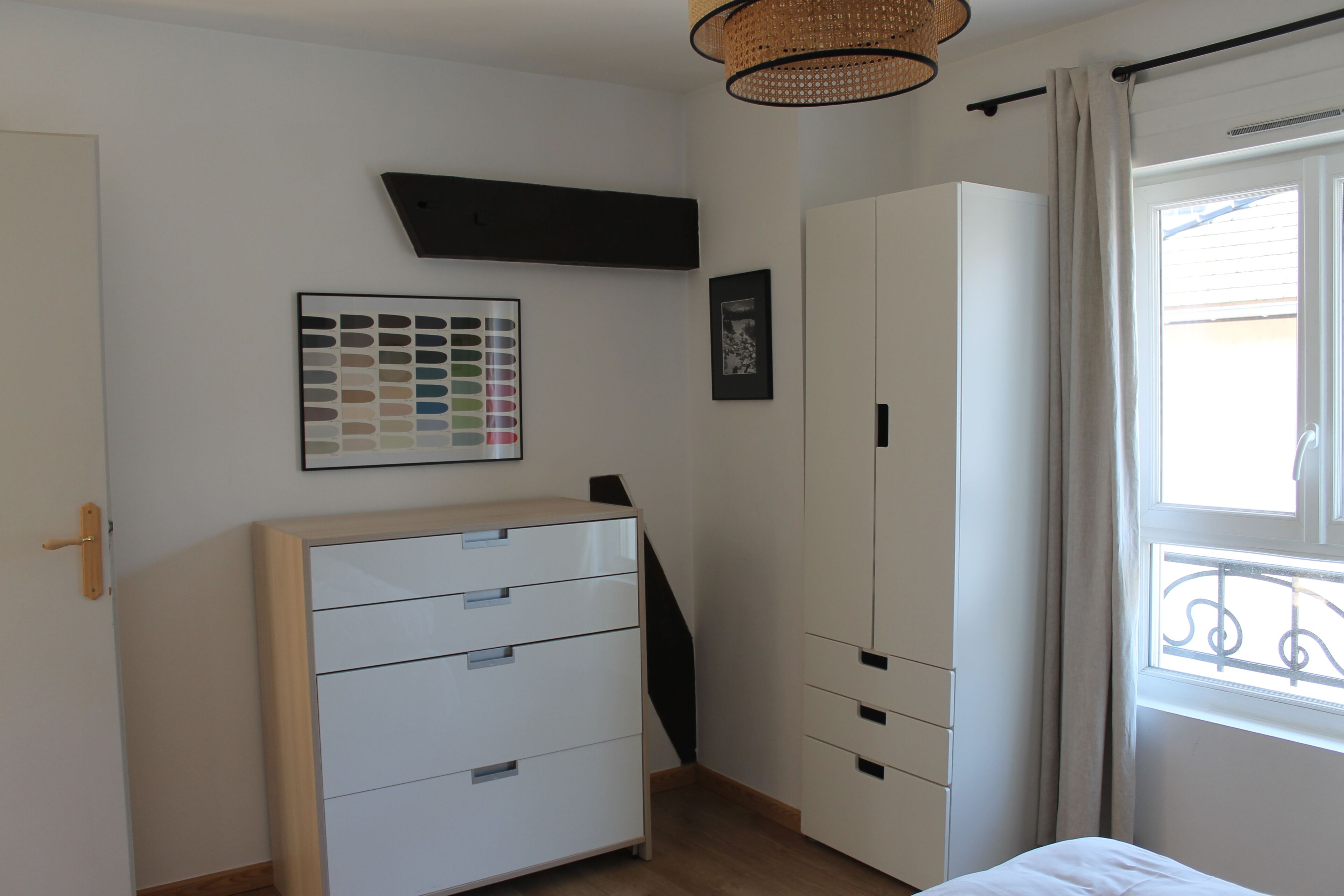 Una camera da letto con un letto, un armadio, una cassettiera, uno scaffale a muro e una finestra con tende.
