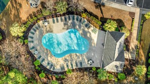 An aerial view of a swimming pool with lounge chairs and a covered area, surrounded by landscaped gardens and a parking lot. - Golf Course Views, 2-bed, 2-bath Condo, Barefoot Resort | Ironwood - 834 (North Myrtle Beach)