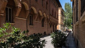 Une ruelle étroite bordée d’un bâtiment en briques, doté de fenêtres et de portes en arc de cercle.