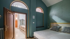 Une chambre avec un lit, deux coussins à motifs, une porte en bois et une vue sur un coin repas, visible à travers une porte ouverte.
